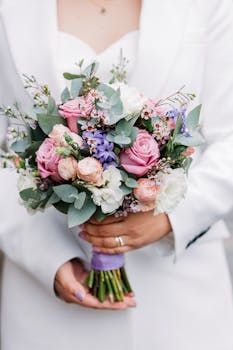 Beautiful bridal bouquet featuring pink roses, eucalyptus, and lavender flowers held by a bride in white.